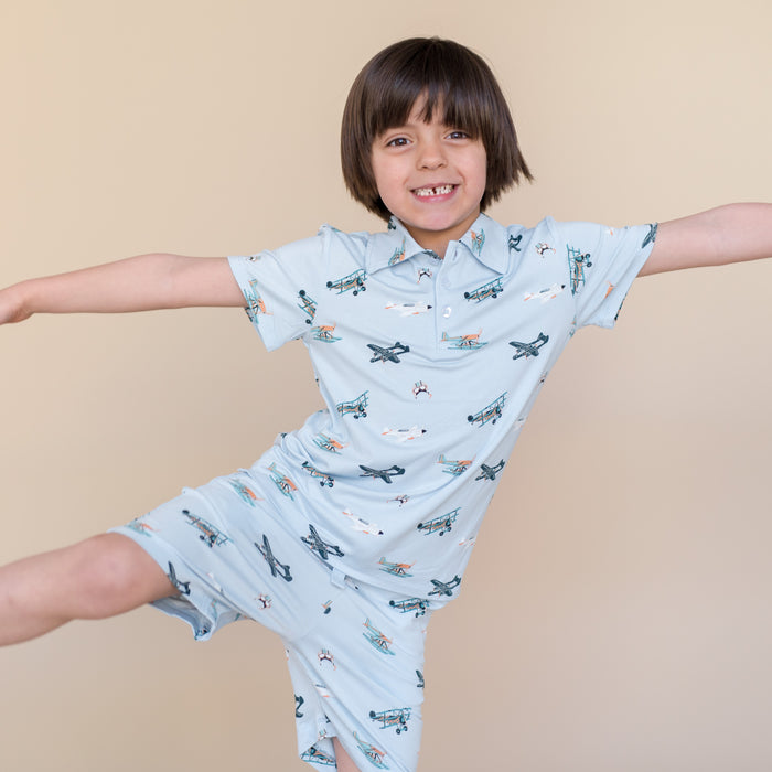 Young smiling boy stretching out wearing the Toddler Short Sleeve Polo in Take Off with matching drawstring shorts
