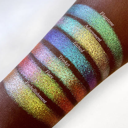 Top angled arm swatches on deep skin tone of Trinket Glitter Multichrome Eyeshadow shifts compared to Flagstone, Adornment, Etched, Flare and Embellishement