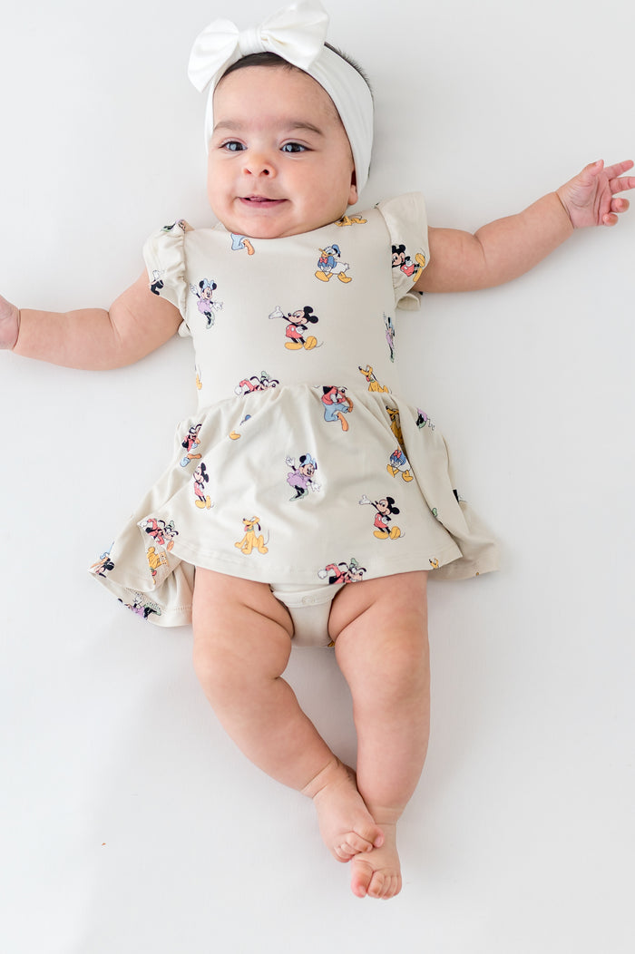 Baby wearing a twirl bodysuit dress with mickey and friend character pattern and white bow