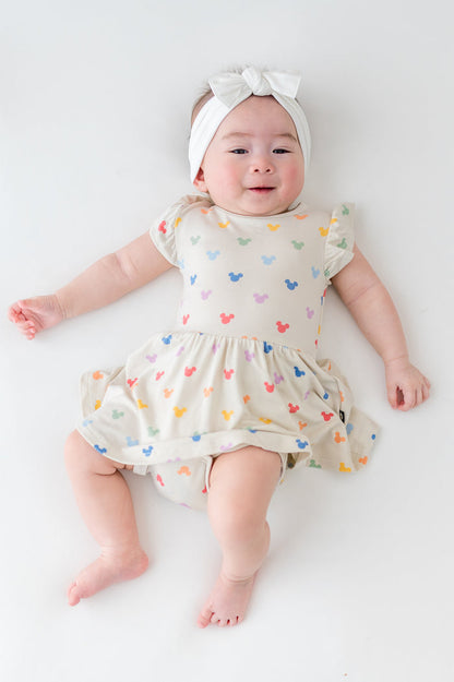 Baby in a twirl dress with built in bodysuit in a colorful pattern of mickey heads