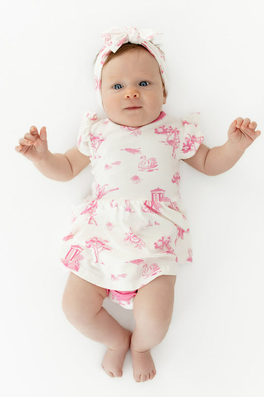 Close up of infant wearing the Twirl Bodysuit Dress in Toile Ballet with matching bow