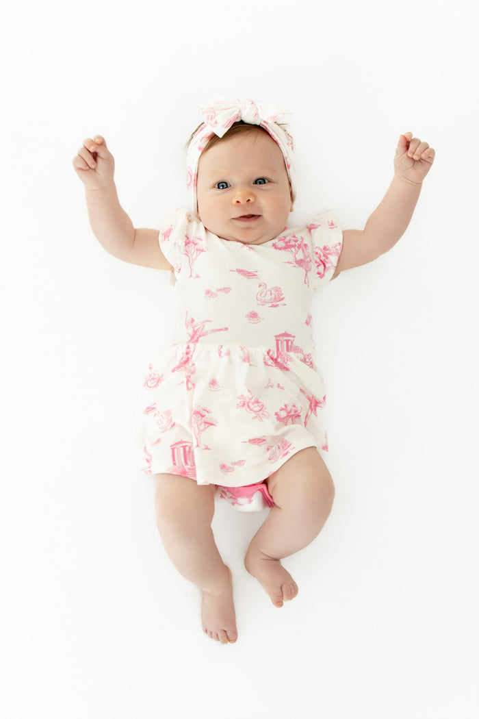 Infant baby wearing the Twirl Bodysuit Dress in Toile Ballet with matching bow