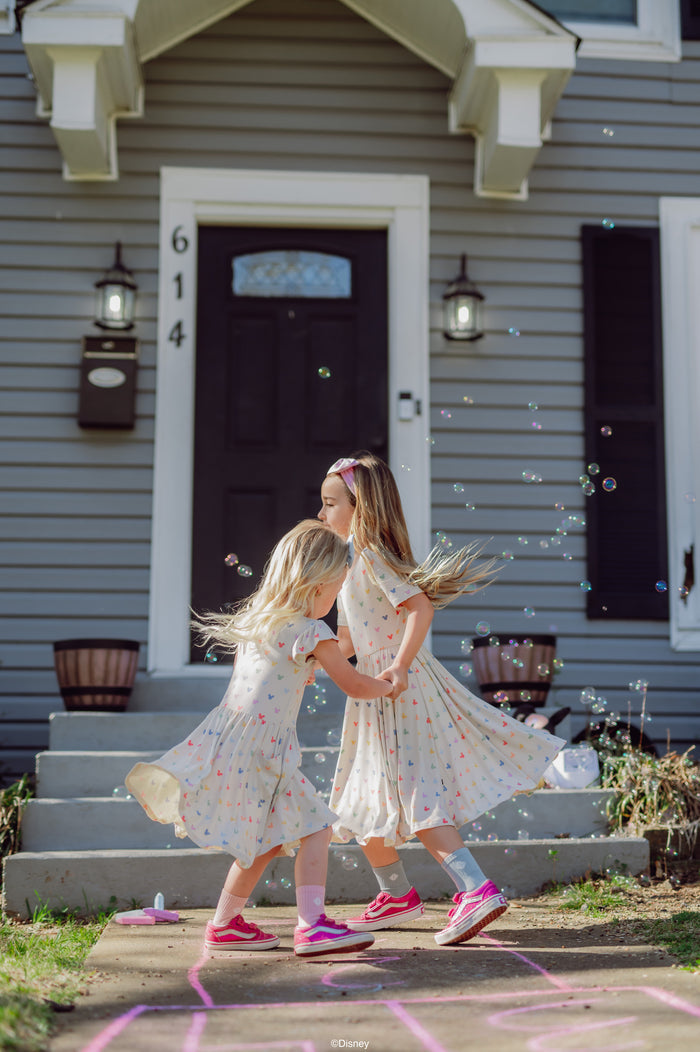 Two young girls in dresses playing with bubbles outside a house.