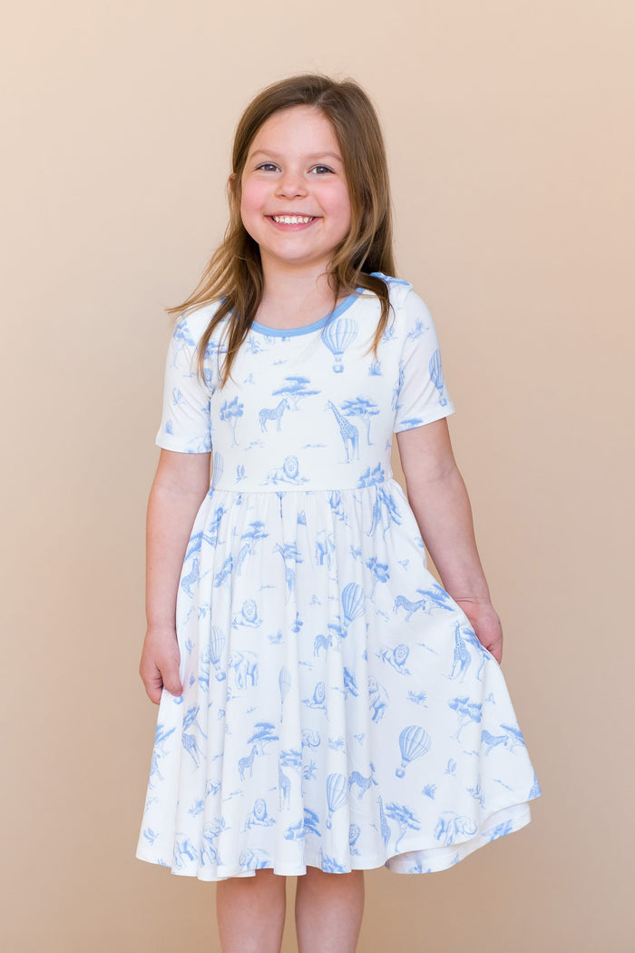 Smiling girl modeling the Twirl Dress in Toile Safari holding the skirt out at the side