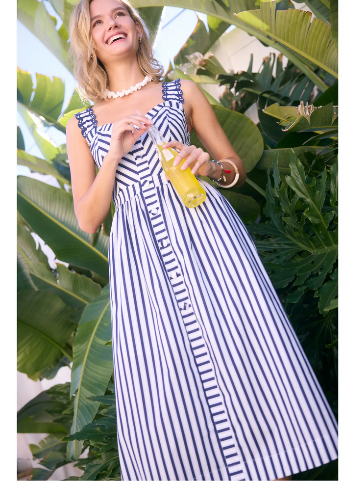 skies are blue United We Stand Stripe Midi Dress - Navy Woman in a striped dress holding a drink among tropical plants