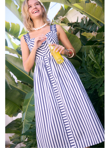 skies are blue United We Stand Stripe Midi Dress - Navy Woman in a striped dress holding a drink among tropical plants