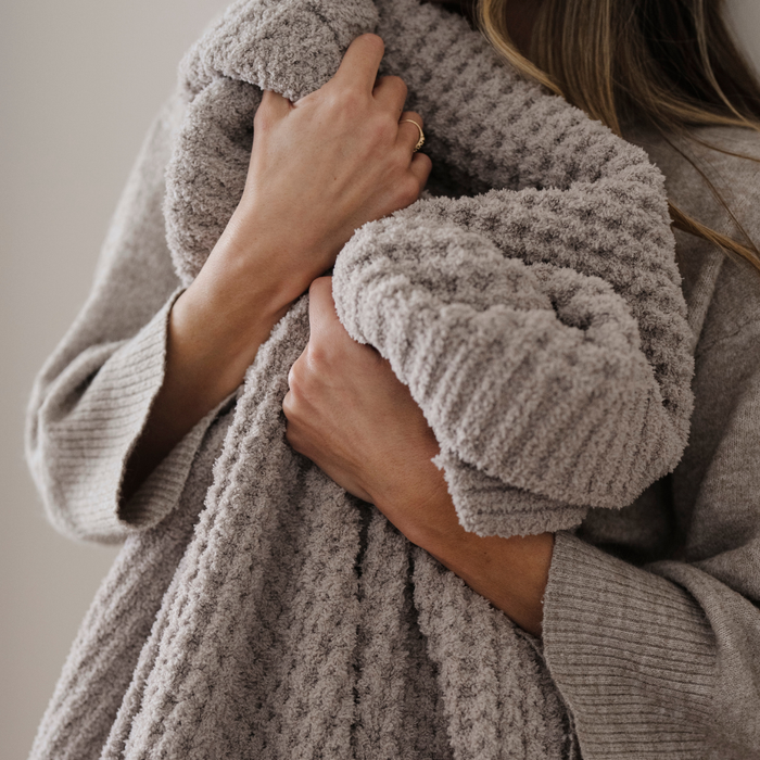 A light tan blanket that is a waffle knit blanket. This luxury blanket is a Saranoni blanket and is super cozy. It can be used for home decor, relaxing, gifting.