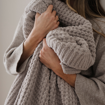 A light tan blanket that is a waffle knit blanket. This luxury blanket is a Saranoni blanket and is super cozy. It can be used for home decor, relaxing, gifting.