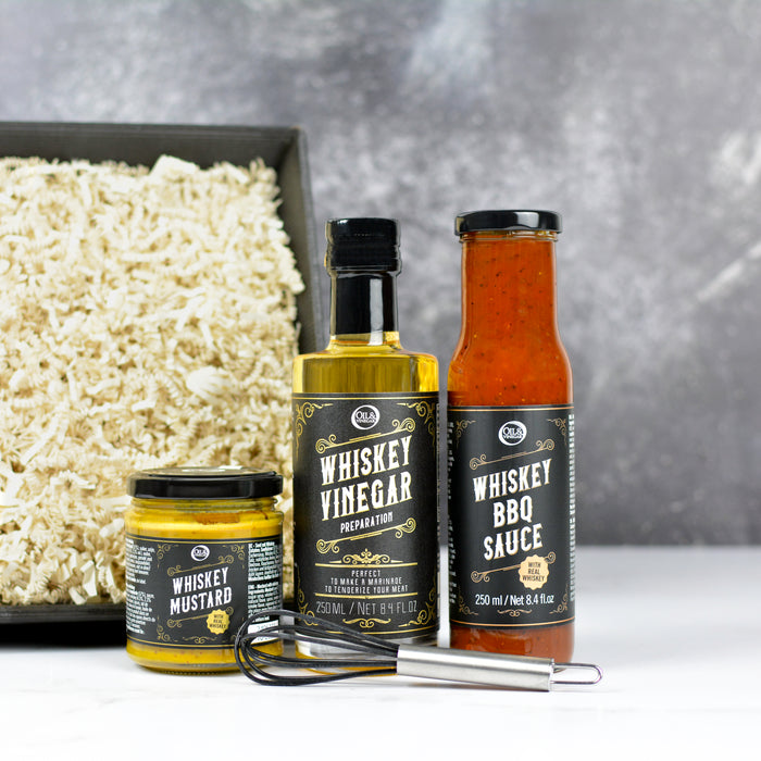 Three bottles of whiskey-based condiments with a gray background and black ribbed box