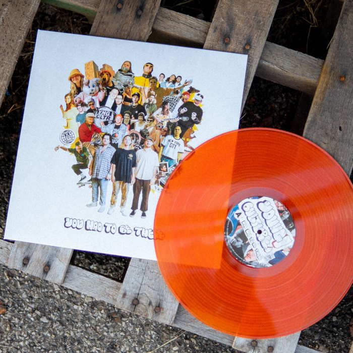 A vibrant Orange Ruby Marble Vinyl from Young Culture rests on a white album cover with a collage of people in diverse outfits and poses, arranged on a wooden pallet outdoors. The album is titled You Had to Be There.